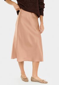 Satin midi skirt in soft beige with an elastic waistband, flowing silhouette, and ankle-length hem, paired with light brown flats featuring studs.