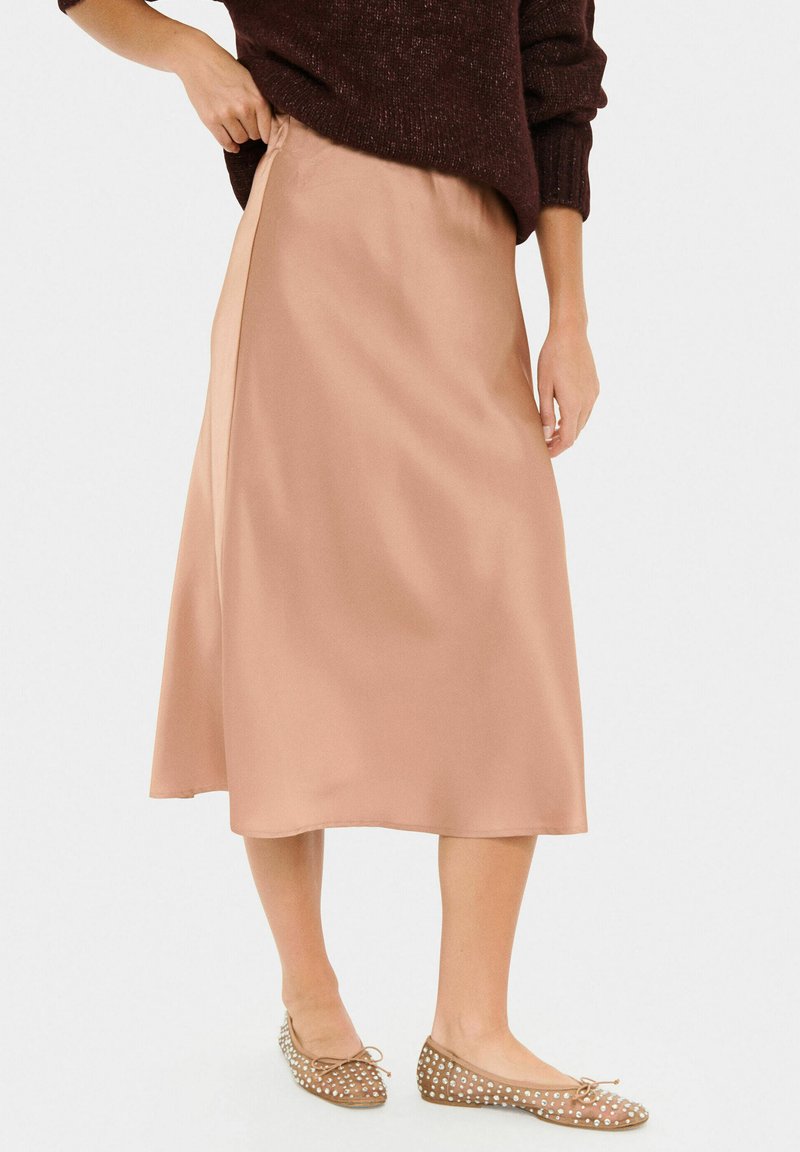 Satin midi skirt in soft beige with an elastic waistband, flowing silhouette, and ankle-length hem, paired with light brown flats featuring studs.
