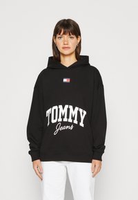 Felpa nera con cappuccio, caratterizzata da un logo bianco "TOMMY Jeans" e un piccolo patch geometrico colorato sul petto. Vestibilità ampia con maniche lunghe.