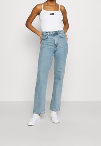 Light blue high-waisted jeans made of denim, featuring a straight-leg design. Paired with a white tank top and white sneakers.