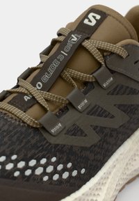 Gray and brown athletic shoe featuring a textured mesh upper, prominent logo, and hexagonal ventilation details on the side.