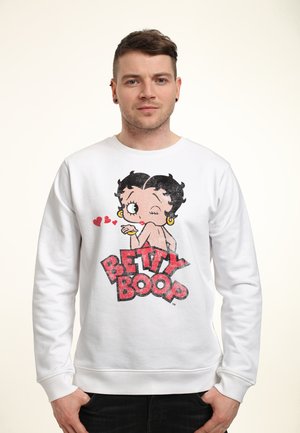 Biała bluza z kolorową grafiką przedstawiającą Betty Boop, z czarnymi włosami, złotymi kolczykami w kształcie kół oraz czerwonymi ustami, nad odważnym napisem "BETTY BOOP".