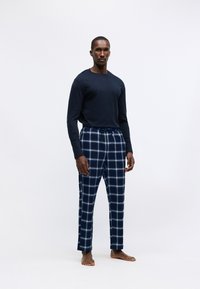 Muška tamnoplava majica dugih rukava u kombinaciji sa plavim kariranim pidžama hlačama. Hlače imaju bijeli karirani uzorak, elastičnu traku u struku i flanelastu teksturu.