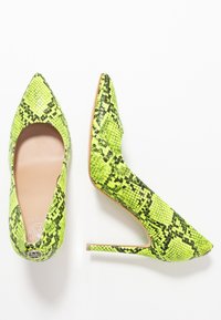 Talons aiguilles à bout pointu en faux python néon vert, présentant une texture brillante, un talon aiguille et un discret accent logo à l'arrière.