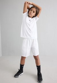 White athletic shirt and shorts with elastic waistband. Black Nike logo on shirt. Black socks and shoes complete the outfit.