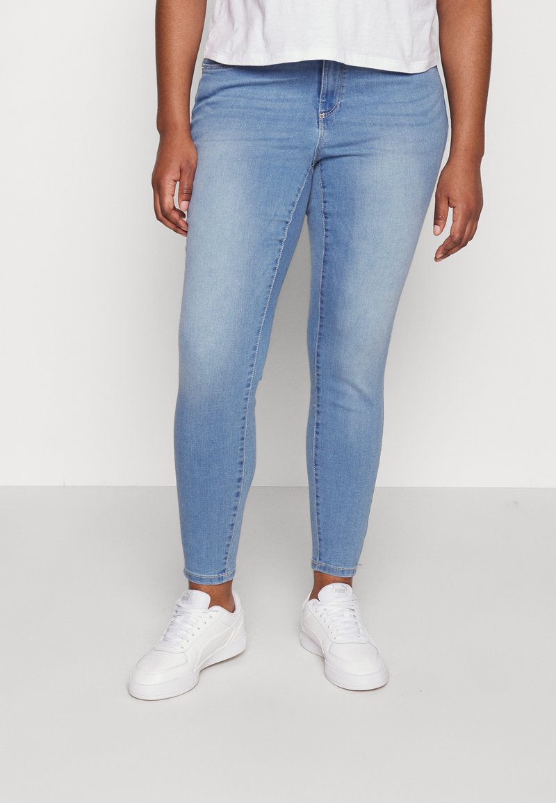Jeans skinny de un albastru deschis, din țesătură de denim, având un design ajustat, talie standard și croială până la gleznă, asortați cu adidași albi.