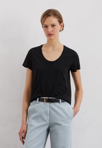 Czarny t-shirt z krótkim rękawem i okrągłym dekoltem, w zestawieniu z jasnoniebieskimi spodniami i czarnym paskiem z złotą klamrą.