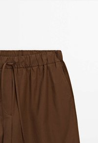 Pantalon marron avec taille élastique, cordon de serrage et poches latérales, visible de la taille à mi-cuisse sur fond blanc.