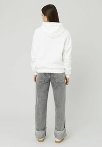 Sweatshirt à capuche blanche avec une coupe décontractée, associé à un jean gris taille haute avec une jambe droite et des poignets repliés.