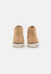 Zapatillas altas de ante en tono marrón con punta redonda y suelas de goma blanca. Presentan un logo circular en el talón exterior y detalles en franjas negras.