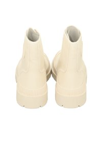 Cream-colored high-top shoes with a canvas upper, curved heel, and textured rubber sole, featuring minimalistic design and no visible branding.
