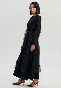 Must kihtidega kleit läbipaistvate tülldetailidega, pikkade varrukatega, vöökinnitusega ja pahkluuni ulatuva äärega. Kandmiseks mustad terava ninaga kontsakingad.