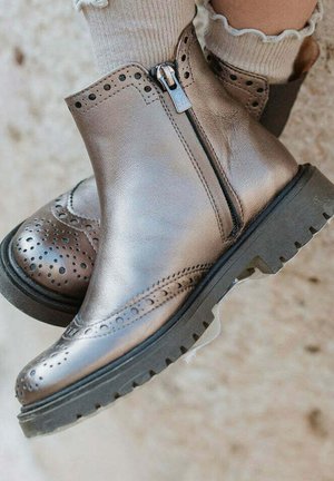 Botas de tobillo de cuero bronce con detalles de brogue, cierre con cremallera lateral, suela de goma texturizada y acabado suave.