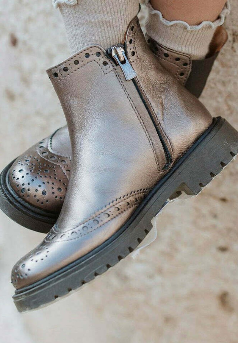 Botas de tobillo de cuero bronce con detalles de brogue, cierre con cremallera lateral, suela de goma texturizada y acabado suave.