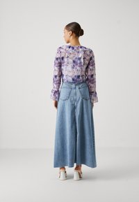 Floral sheer long-sleeve blouse in purple and light pink paired with a high-waisted denim maxi skirt. Accent ruffles on blouse sleeves.