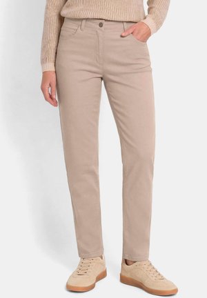Beige Hose mit geradem Bein, getragen mit passenden beigen Sneakern und einem hellbraunen strukturierten Pullover, eine Hand in der Tasche.