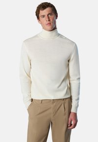 Suéter de cuello alto crema de punto suave, diseño ajustado con mangas largas, combinado con pantalones beige de corte entallado. Textura suave, detalles mínimos.