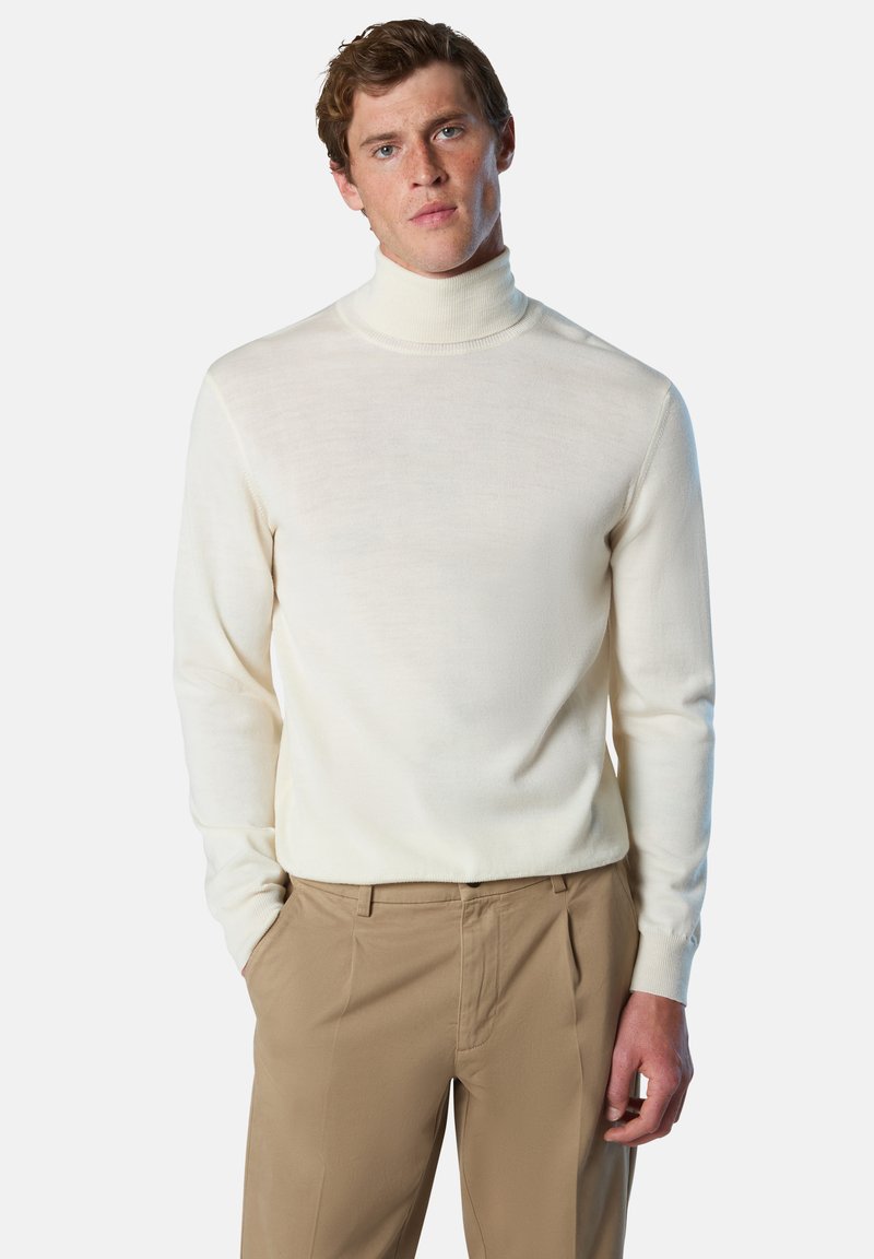 Suéter de cuello alto crema de punto suave, diseño ajustado con mangas largas, combinado con pantalones beige de corte entallado. Textura suave, detalles mínimos.
