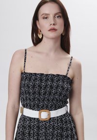 Zwarte jurk met witte bloemenborduursels, aansluitend bovenlijf, spaghettibandjes en een brede witte riem met een getextureerde rechthoekige gesp.