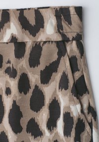Nærbillede af beige og sort leopardprintstof med en taljebånd og detaljer med sidelomme på tøj.