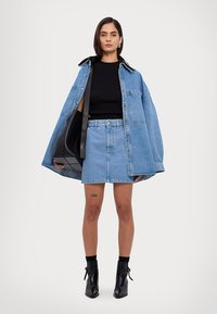 Svijetloplavi oversized traper jakna preko crnog rebrastog pulovera i traper suknje. Crne gležnjače upotpunjuju izgled. Istaknuta tetovaža na nozi.