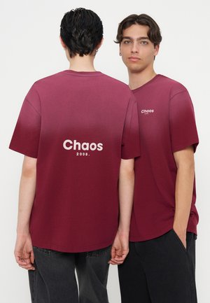 Deux jeunes hommes portant des t-shirts rouge foncé assortis avec "Chaos 2008" imprimé, l’un face et l’autre montrant le design au dos.