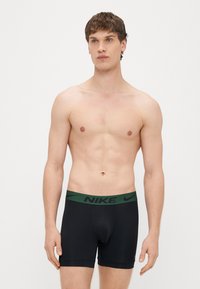 Mustad bokserid rohelise Nike logoga vöökohaga. Kangas tundub sile ja veniv, loodud mugavuse ja sobivuse tagamiseks.