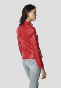 Punane nahast jakk, kujult lõigatud, kõrge krae ja külgedel nupukaunistused. Stiilitud helesiniste teksadega. Sile tekstuur ja kohandatud vorm.