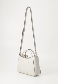 Sac à main texturé blanc avec deux poignées supérieures et une bandoulière amovible. Équipé de quincaillerie en ton doré et d'un design minimaliste avec des accents subtils.