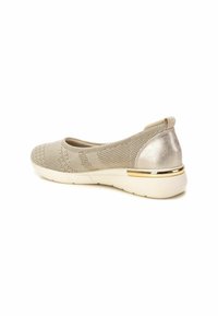 Zapato beige sin cordones con textura de punto, acento metálico plateado en el talón y suela blanca acolchada. Perforaciones decorativas visibles.