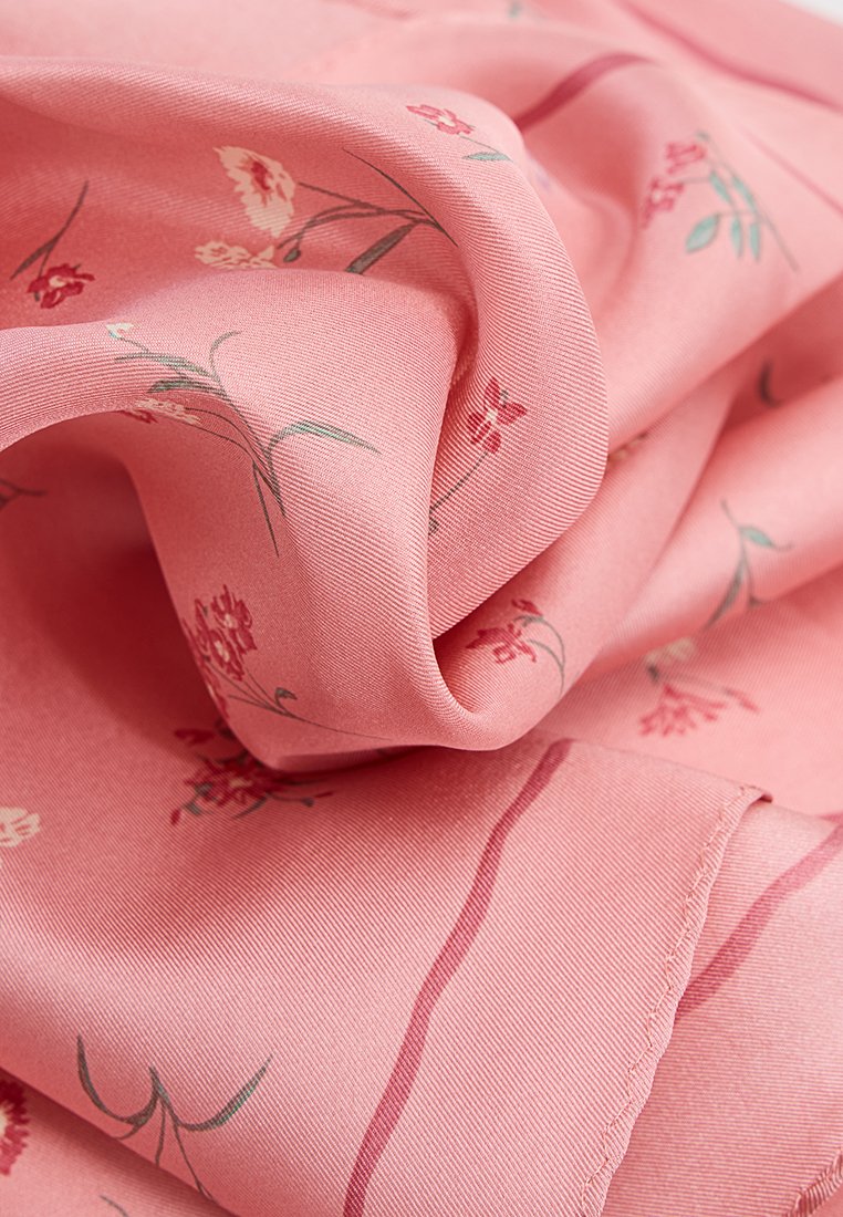 Rosa, blumengemusterter Stoff, weiche Textur, mit kleinen roten und grünen Blumen auf einer glatten, satinähnlichen Oberfläche mit zarten Falten.