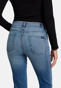 Blauwe spijkerbroek van denim met een iets lichtere blauwe wassing, voorzien van twee achterzakken en een middelhoge taille. Glad textuur met stikseldetails.
