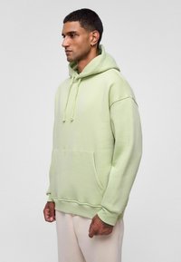Lichtgroene hoodie met een grote voorzak, trekkoordcapuchon en geribbelde manchetten. Zachte textuur en comfortabele pasvorm.