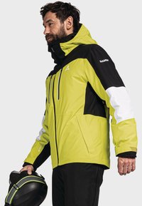 Giacca da uomo, verde lime brillante con dettagli neri e bianchi, realizzata in materiale impermeabile. Presenta un colletto alto e molteplici tasche con zip.