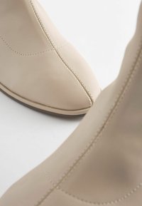 Beige ankle boots made of smooth leather with a pointed toe, featuring subtle stitching and a low heel, showcasing a minimalist design.