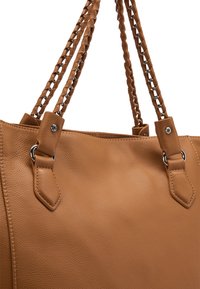 Borsa a spalla in pelle tan con manici intrecciati, dettagli in argento e forma strutturata. Texture liscia con due manici superiori e accessori decorativi.