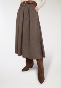 Gonna midi a quadri marrone con pieghe, caratterizzata da una cintura marrone con fibbia rotonda. Abbinata a stivaletti alla caviglia in pelle scamosciata marrone.