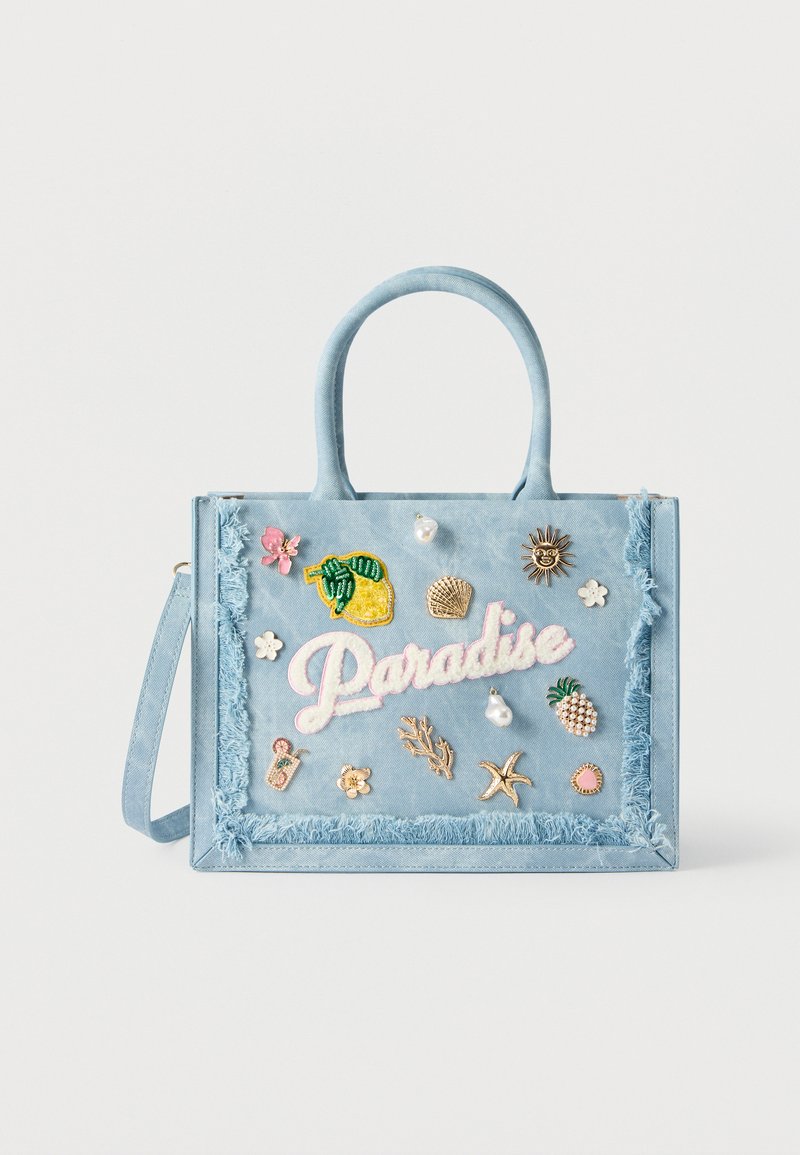 Bolso azul claro con bordes deshilachados, decorado con pines y parches tropicales que incluyen limón, piña, sol, estrella de mar y texto "Paraíso".