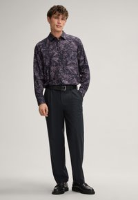 Langarm-Hemd mit einem dunkellila Blattmuster. Kombiniert mit dunklen Hosen und polierten schwarzen Schuhen.