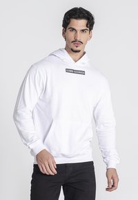Sudadera blanca con un bolsillo tipo canguro en el frente, capucha ajustable con cordón, y un detalle de logotipo rectangular negro en el pecho.