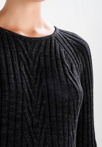 Primo piano di una persona che indossa un maglione nero a costine con un motivo testurizzato e un collo rotondo, che mette in evidenza i dettagli del tessuto.