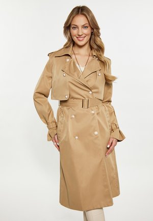 Beige trench coat, dupla gombolású dizájnnal, selymes textúrával, díszvarrott gombokkal és övvel ellátott derékrésszel. Rövidített kabát stílusú.