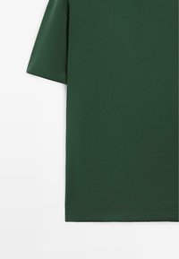 T-shirt vert foncé à manches courtes avec un design sobre, présenté sur un fond blanc.