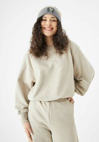 Lichtbeige sweatshirt met oversized mouwen, gecombineerd met bijpassende sweatpants. Grijs en tan gestreepte beanie met een geborduurd logo.