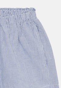 Blå og hvite stripete shorts med elastisk midjebånd, rynket tekstur og sidelommer. Lett materiale med vertikale linjer.