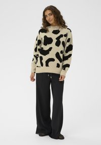 Bežs džemperis ar melnu abstraktu leoparda rakstu, ar plašu kaklu un ribotām piedurknēm, kombinēts ar melnām platām biksēm.