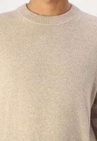 Beige kötött pulóver kerek nyakkal, puha, texturált anyagból készült. Bordázott gallérral és sima felülettel rendelkezik.