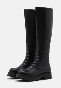Botas negras hasta la rodilla, de cuero suave, con detalles acolchados, suela plana y cremallera lateral para mayor facilidad.