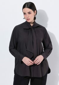 Sort langærmet skjorte med sløjfe-collier, lavet af glat stof. Har frontknaplukning og en let buet kant.