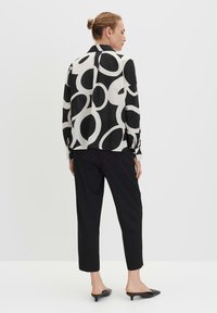 Blusa a strisce bianco e nero con grandi motivi circolari, maniche lunghe, polsini con bottoni e taglio sartoriale, abbinata a pantaloni neri.